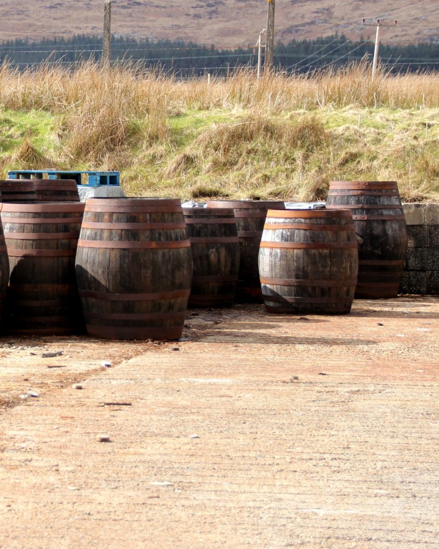 Weathered whiskey casks stacked outdoors near a Scottish coastline