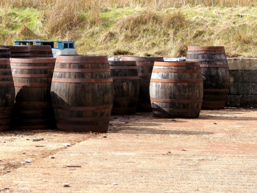 Weathered whiskey casks stacked outdoors near a Scottish coastline
