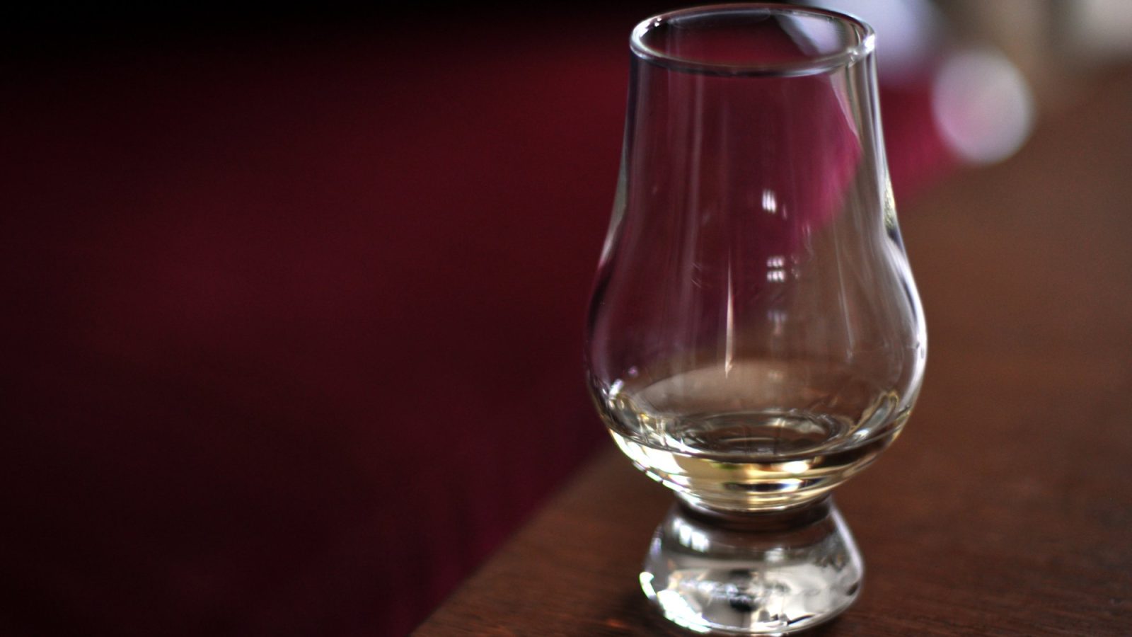 Amber whiskey in a Glencairn glass on a dark wood bar with warm bokeh lighting