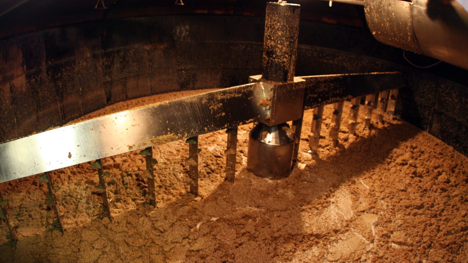 Interior of a mash tun with grain mash being stirred by rakes